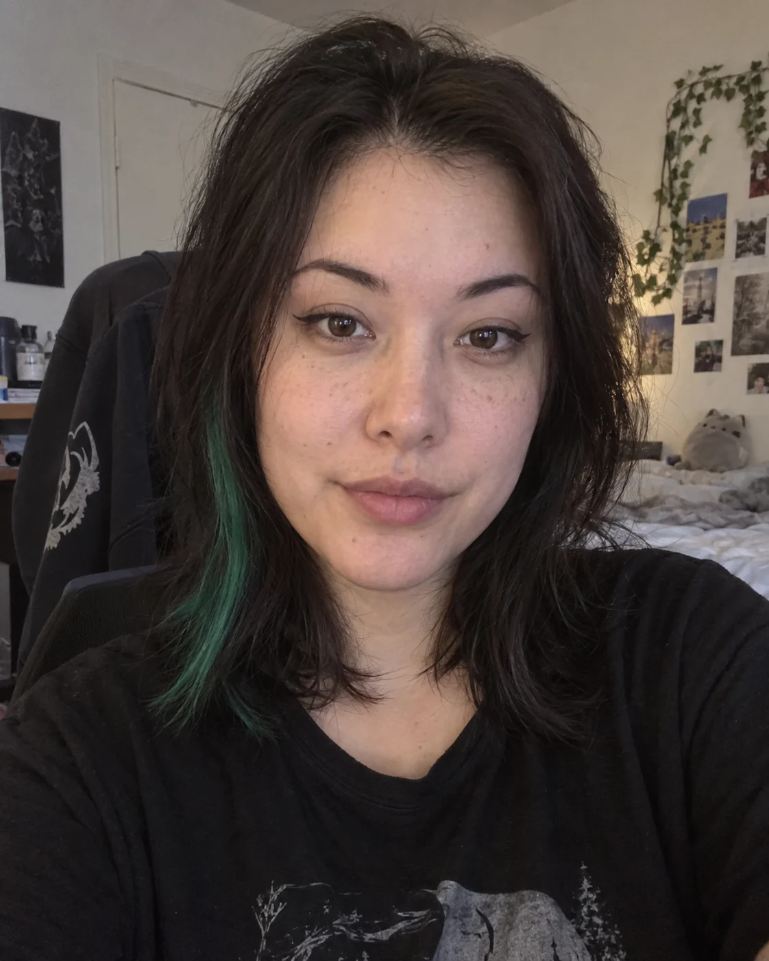 Explanatory photo: the same adult on a different day takes a front-camera selfie at home, hair down, wearing a black T-shirt, face centered and looking at the lens.